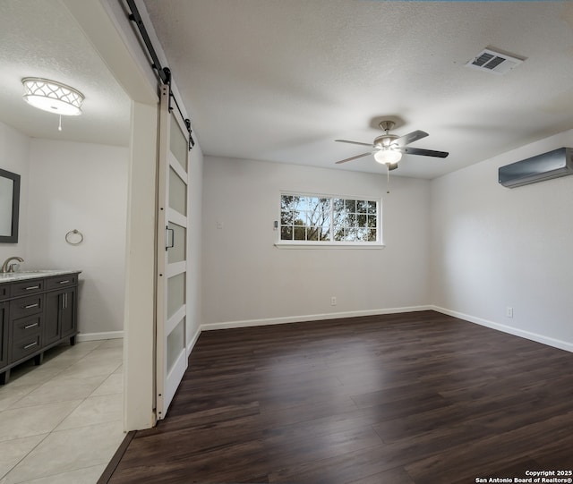 empty room featuring light hardwood / wood-style flooring, ceiling fan, a textured ceiling, a barn door, and an AC wall unit