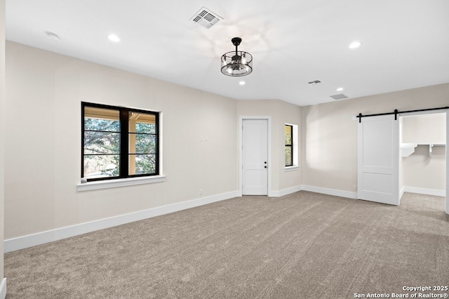 unfurnished room with a barn door, plenty of natural light, and light colored carpet