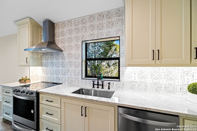 kitchen with sink, wall chimney range hood, stainless steel appliances, light stone countertops, and cream cabinetry