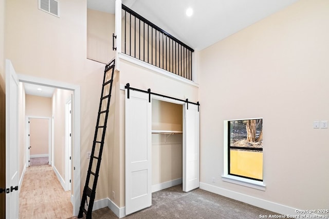 unfurnished bedroom featuring a barn door, a towering ceiling, light carpet, and a closet