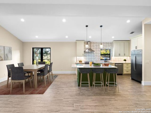 kitchen featuring a kitchen island, decorative backsplash, hanging light fixtures, fridge, and wall chimney range hood