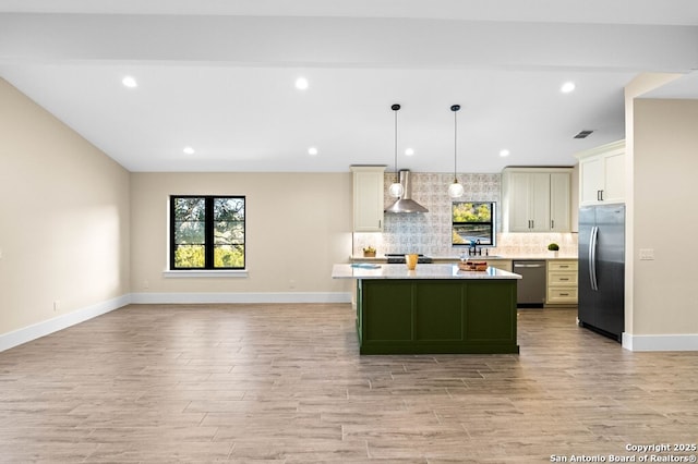 kitchen with a kitchen island, pendant lighting, tasteful backsplash, stainless steel appliances, and wall chimney exhaust hood