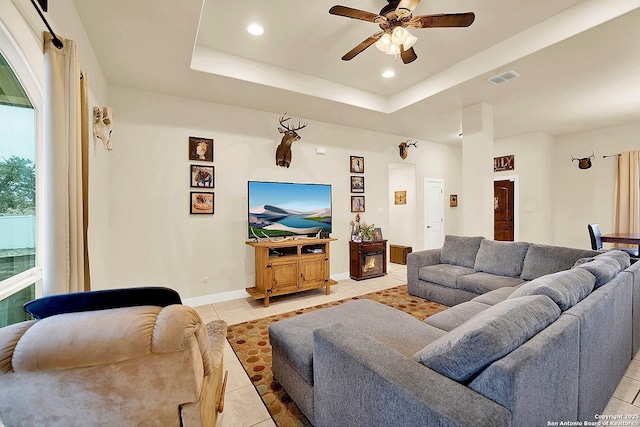 living room with light tile patterned floors, a tray ceiling, and ceiling fan