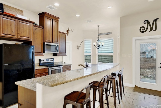 kitchen with a kitchen breakfast bar, appliances with stainless steel finishes, light stone counters, and decorative light fixtures