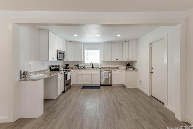 kitchen with appliances with stainless steel finishes, white cabinetry, sink, light hardwood / wood-style floors, and light stone countertops