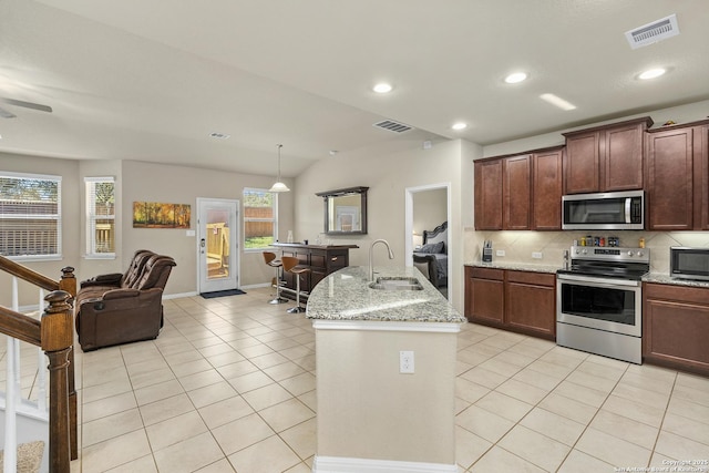 kitchen featuring sink, light tile patterned floors, appliances with stainless steel finishes, a kitchen island with sink, and light stone counters