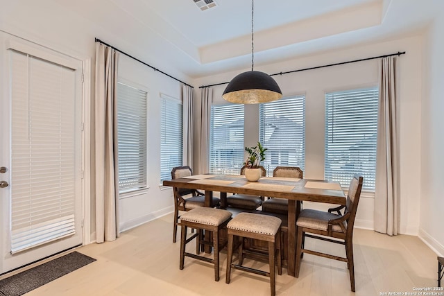 dining room with a tray ceiling, light wood-style floors, visible vents, and a wealth of natural light