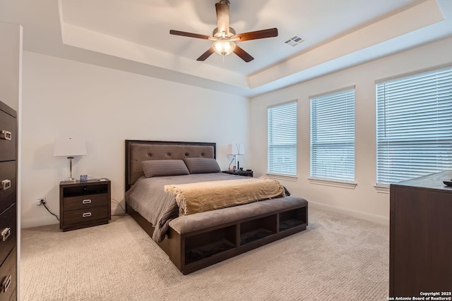 bedroom featuring visible vents, baseboards, ceiling fan, a raised ceiling, and light colored carpet