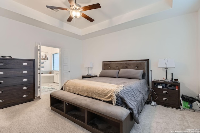 bedroom with a tray ceiling, a ceiling fan, ensuite bathroom, and light carpet