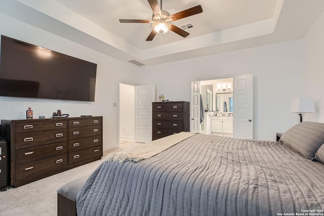 bedroom with ceiling fan, ensuite bathroom, a tray ceiling, and light carpet