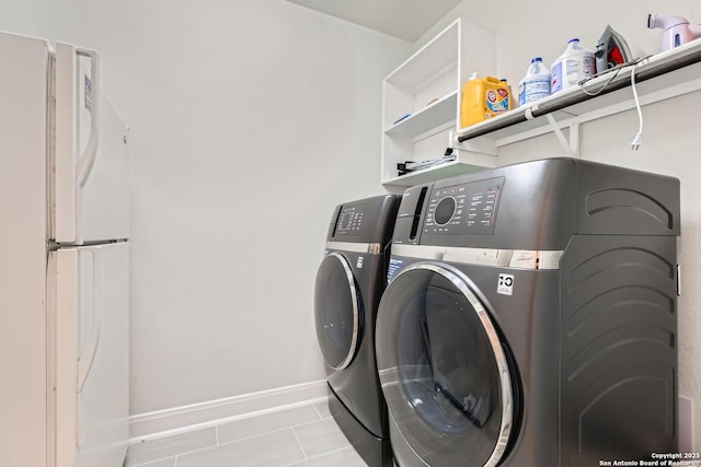 clothes washing area featuring tile patterned flooring, laundry area, independent washer and dryer, and baseboards