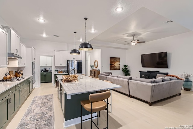 kitchen featuring stainless steel appliances, visible vents, a breakfast bar area, and an island with sink