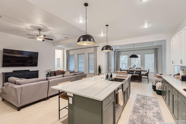 kitchen featuring white cabinetry, an island with sink, sink, hanging light fixtures, and light stone counters