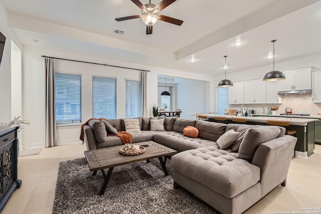 living area with a raised ceiling, recessed lighting, visible vents, and ceiling fan