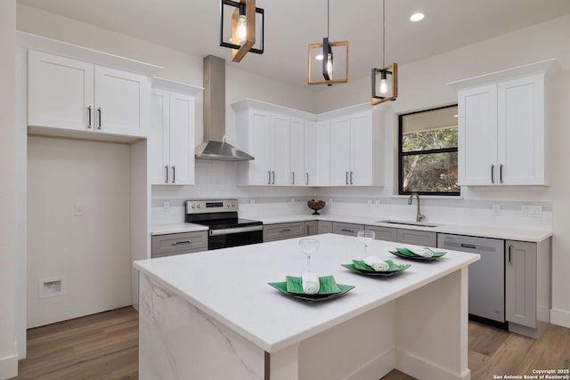 kitchen with wall chimney range hood, sink, hanging light fixtures, stainless steel appliances, and white cabinets