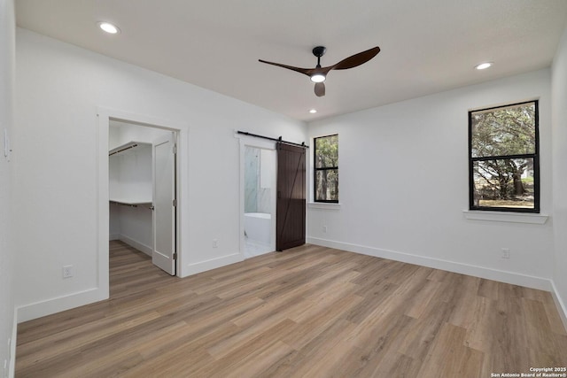 unfurnished bedroom with a spacious closet, light wood-type flooring, a closet, ceiling fan, and a barn door