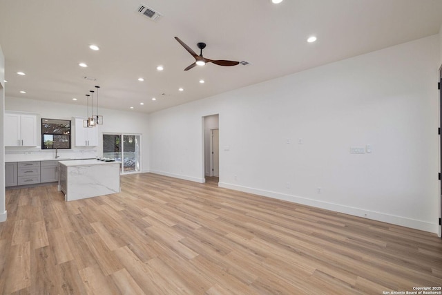 unfurnished living room with sink, ceiling fan, and light wood-type flooring