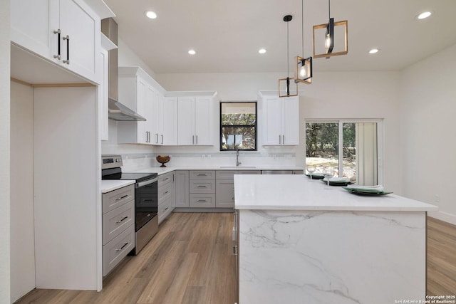 kitchen featuring wall chimney exhaust hood, decorative light fixtures, a center island, electric range, and white cabinets