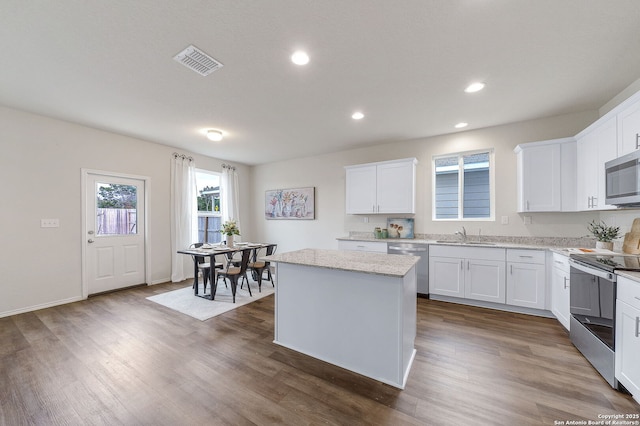 kitchen featuring a kitchen island, white cabinetry, light stone counters, stainless steel appliances, and dark wood-type flooring