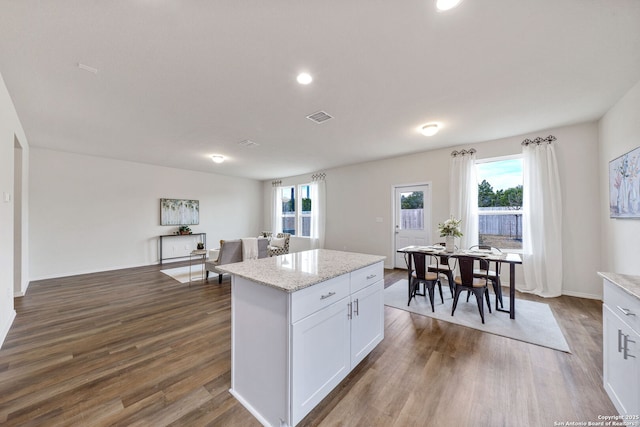 kitchen with white cabinetry, a center island, dark hardwood / wood-style floors, and light stone countertops