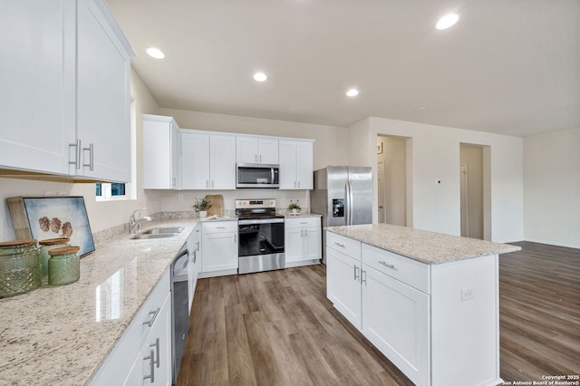 kitchen featuring white cabinetry, a center island, hardwood / wood-style flooring, stainless steel appliances, and light stone countertops