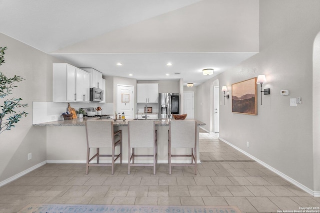 kitchen featuring appliances with stainless steel finishes, a breakfast bar area, white cabinets, kitchen peninsula, and light stone countertops