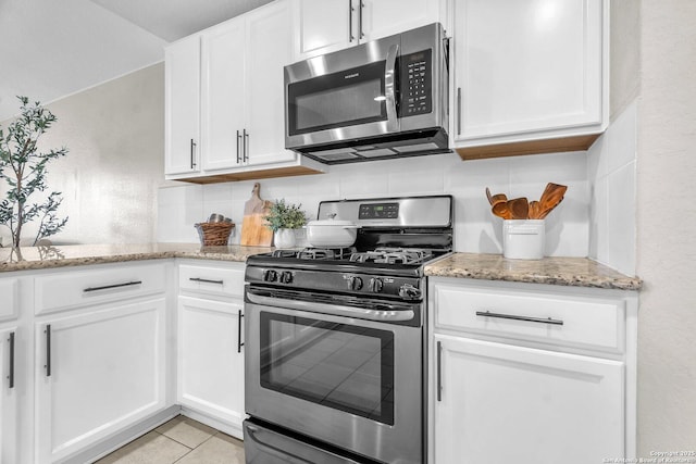 kitchen with white cabinetry, backsplash, light tile patterned floors, light stone counters, and stainless steel appliances