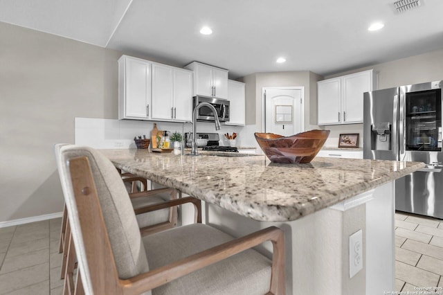 kitchen featuring a breakfast bar, white cabinetry, light stone counters, kitchen peninsula, and stainless steel appliances