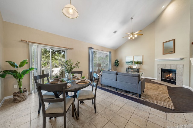 dining space with ceiling fan, high vaulted ceiling, light tile patterned flooring, and a tile fireplace