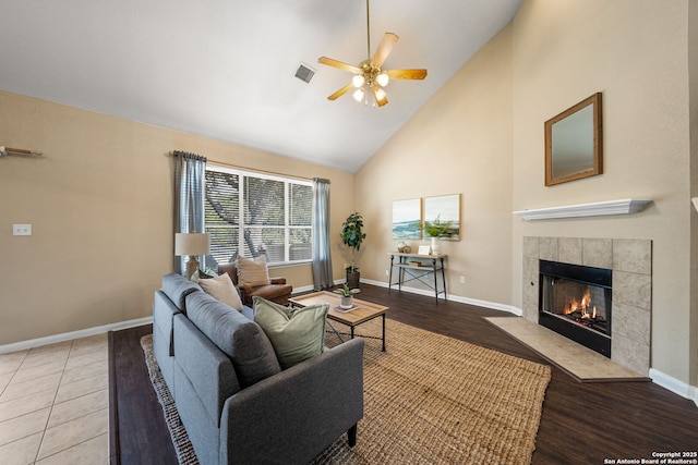 living room featuring ceiling fan, high vaulted ceiling, a tile fireplace, and light hardwood / wood-style flooring