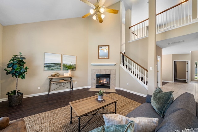 living room featuring a fireplace, ceiling fan, wood-type flooring, and a towering ceiling