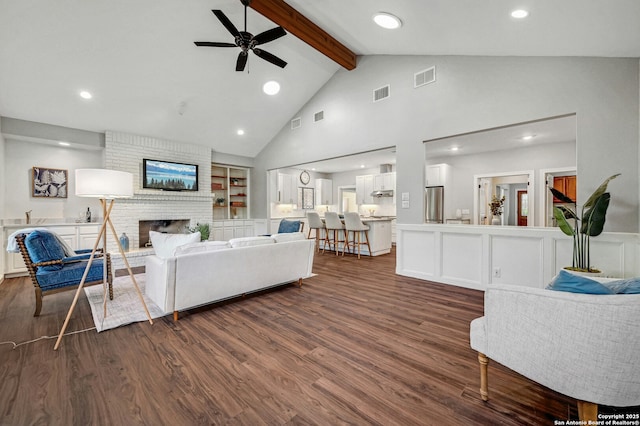 living room with high vaulted ceiling, ceiling fan, a brick fireplace, dark wood-type flooring, and beam ceiling