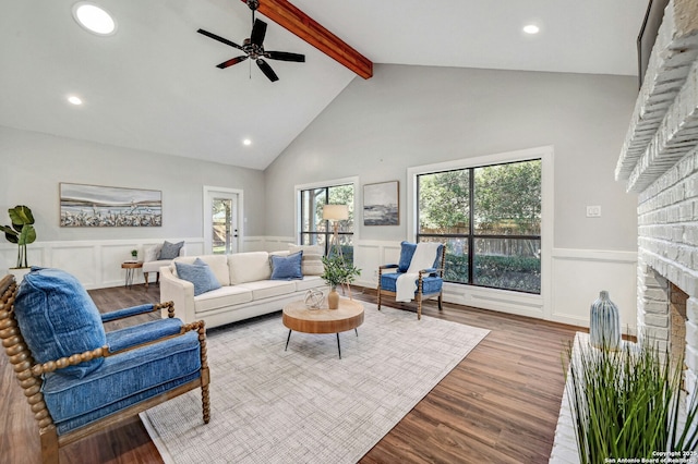 living room featuring ceiling fan, beam ceiling, high vaulted ceiling, a brick fireplace, and light wood-type flooring