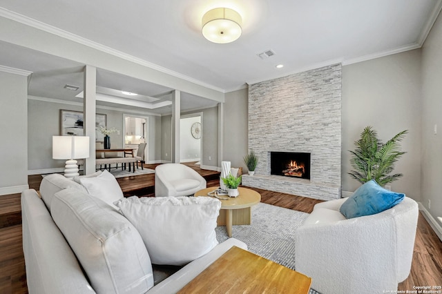 living room with a stone fireplace, ornamental molding, and hardwood / wood-style flooring