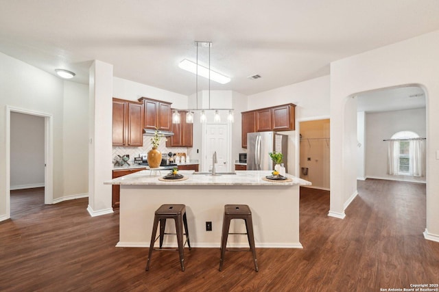 kitchen with hanging light fixtures, sink, stainless steel refrigerator, and a center island with sink