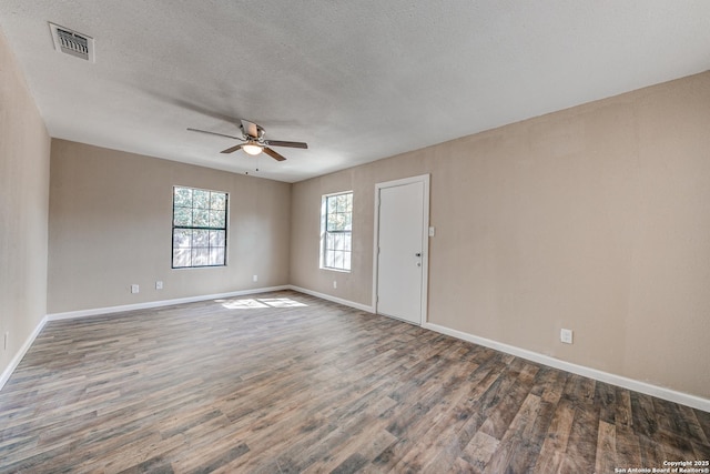 spare room with a ceiling fan, visible vents, dark wood finished floors, and baseboards