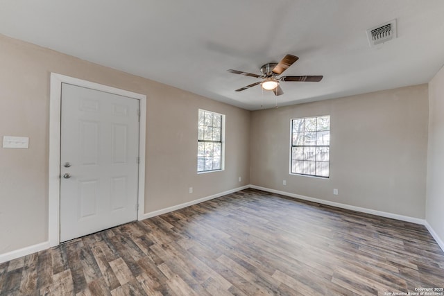 empty room with a healthy amount of sunlight, visible vents, dark wood finished floors, and baseboards