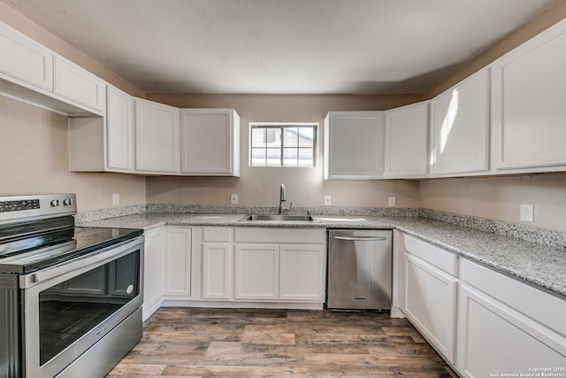 kitchen featuring light stone counters, wood finished floors, stainless steel appliances, white cabinetry, and a sink