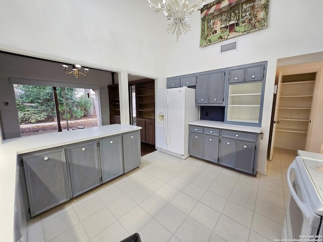 kitchen with light tile patterned flooring, gray cabinets, a notable chandelier, white appliances, and a high ceiling