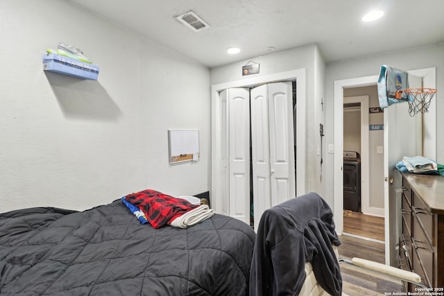 bedroom with washer / clothes dryer, hardwood / wood-style floors, and a closet