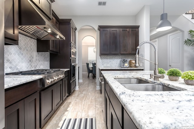 kitchen with decorative light fixtures, range hood, sink, stainless steel gas cooktop, and light stone countertops