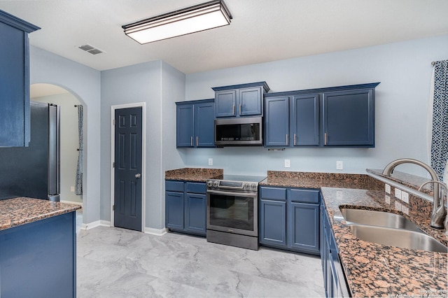 kitchen with stainless steel appliances, sink, blue cabinets, and dark stone counters