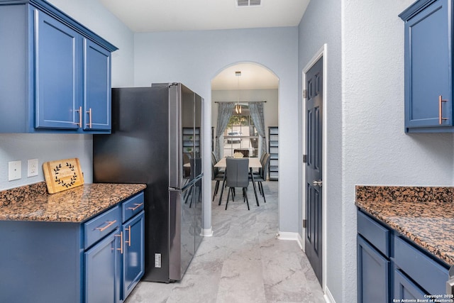 kitchen with blue cabinetry, dark stone countertops, and stainless steel refrigerator with ice dispenser