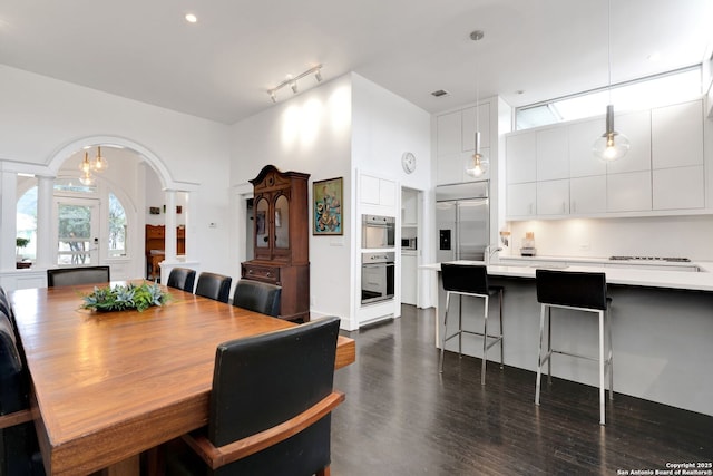 dining area featuring a towering ceiling, dark wood-type flooring, decorative columns, and rail lighting