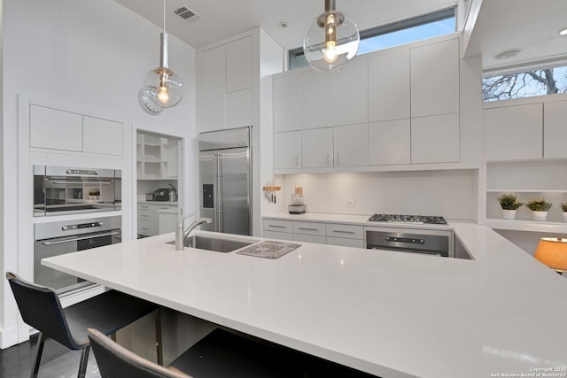 kitchen featuring sink, a high ceiling, white cabinets, decorative light fixtures, and built in fridge