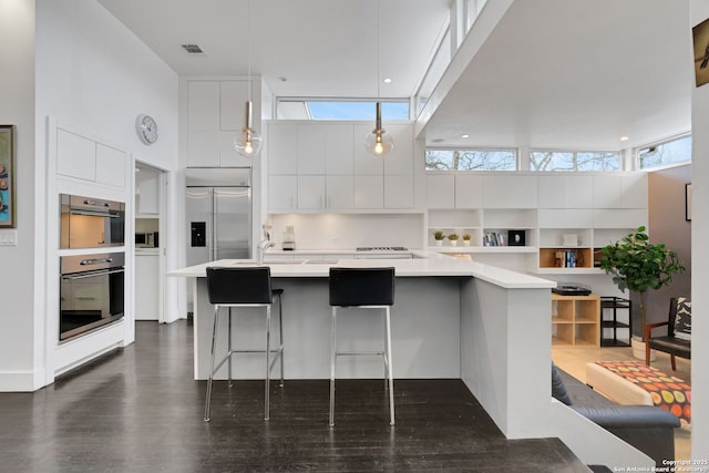 kitchen featuring appliances with stainless steel finishes, white cabinetry, a towering ceiling, a kitchen breakfast bar, and dark hardwood / wood-style floors