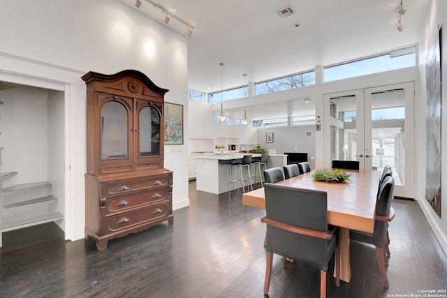 dining space with french doors, a towering ceiling, a healthy amount of sunlight, and dark hardwood / wood-style floors