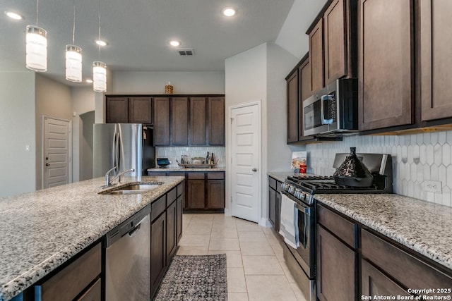 kitchen with stainless steel appliances, light stone countertops, sink, and dark brown cabinets