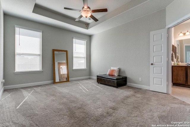 unfurnished bedroom featuring a raised ceiling, connected bathroom, light carpet, and ceiling fan