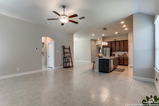 kitchen with stainless steel fridge, a kitchen breakfast bar, ceiling fan, light stone counters, and a center island with sink